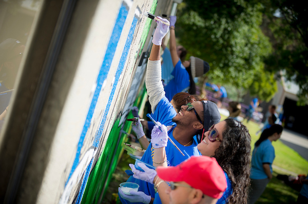 Students Smiling and Painting a Mural on a Wall Outside