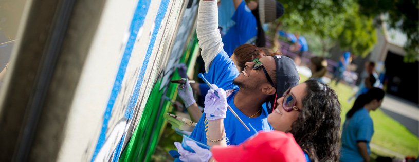 Two Students Painting Mural outdoors on a concrete wall